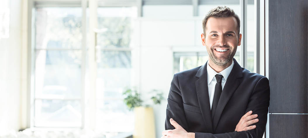 Portrait of happy businessman wearing suit standing with arms crossed in an office, smiling at camera.