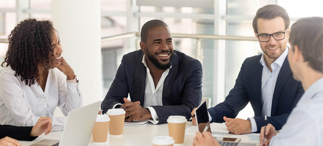 Happy diverse business people talk at group negotiations sit at conference office table, multiracial professional team colleagues negotiate having fun conversation discuss work at corporate meeting
